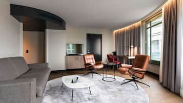 Een moderne woonkamer met een bank, twee leren fauteuils, een salontafel en een eethoek met een tafel en stoelen.