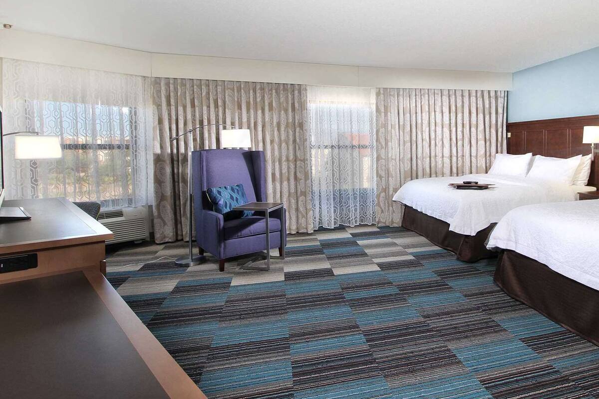 A hotel room with two beds, a desk, a chair, and a television.
