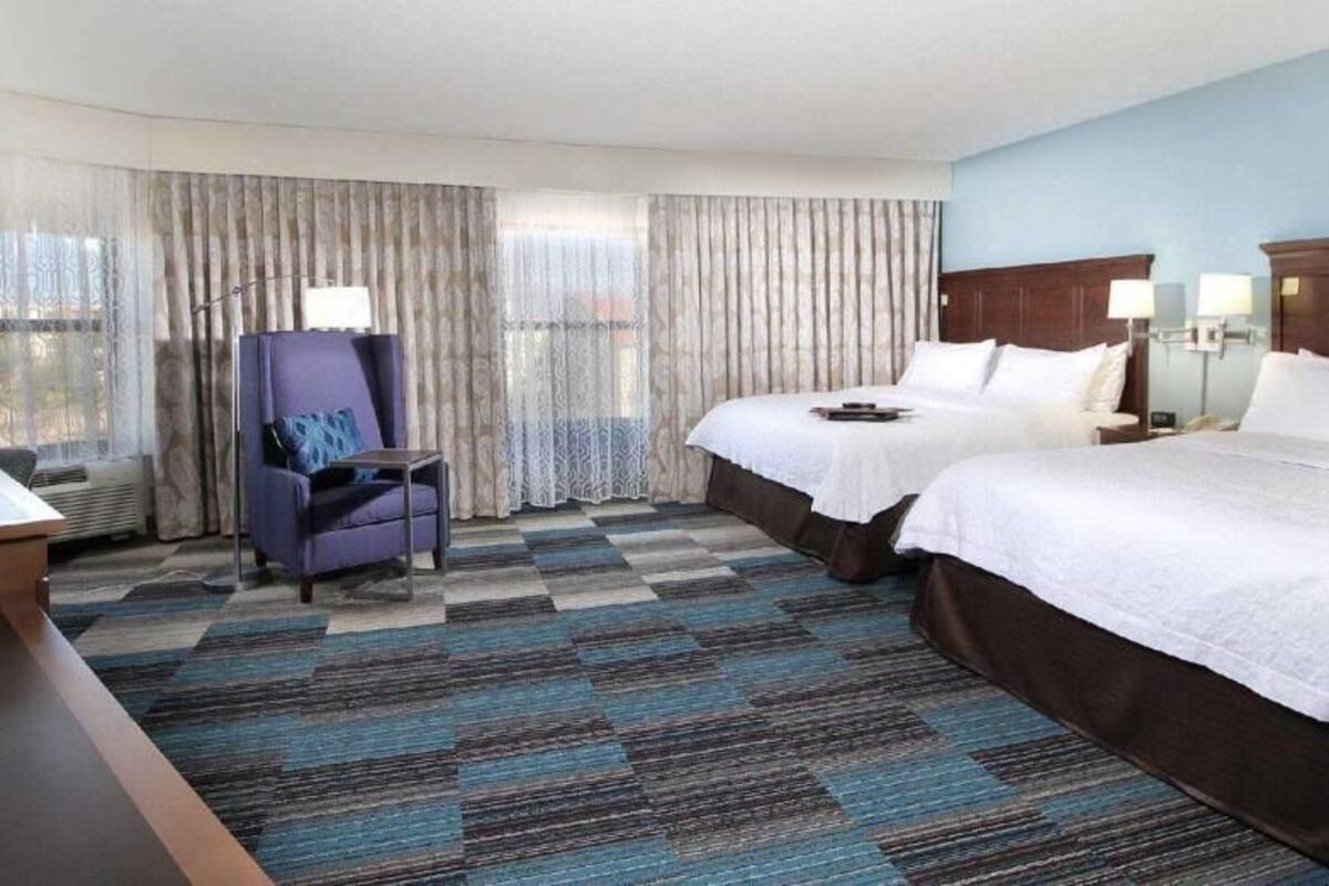 A hotel room with two beds, a desk, a chair, and a television.