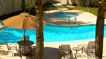 A swimming pool with lounge chairs and an umbrella, surrounded by palm trees and a paved deck.