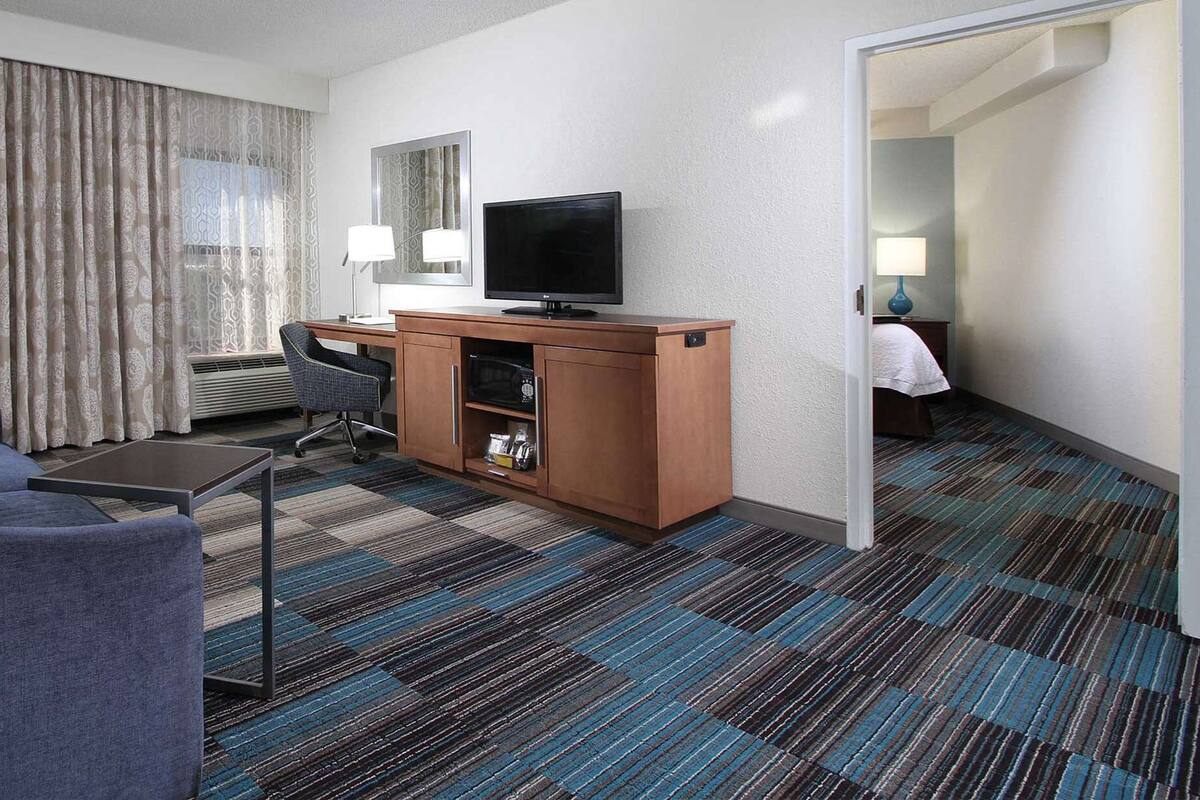 A hotel room with a sofa, a desk, a television, a mirror, and a patterned carpet.