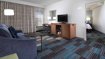 Una habitación de hotel con sofá, escritorio, televisión, espejo y alfombra estampada.