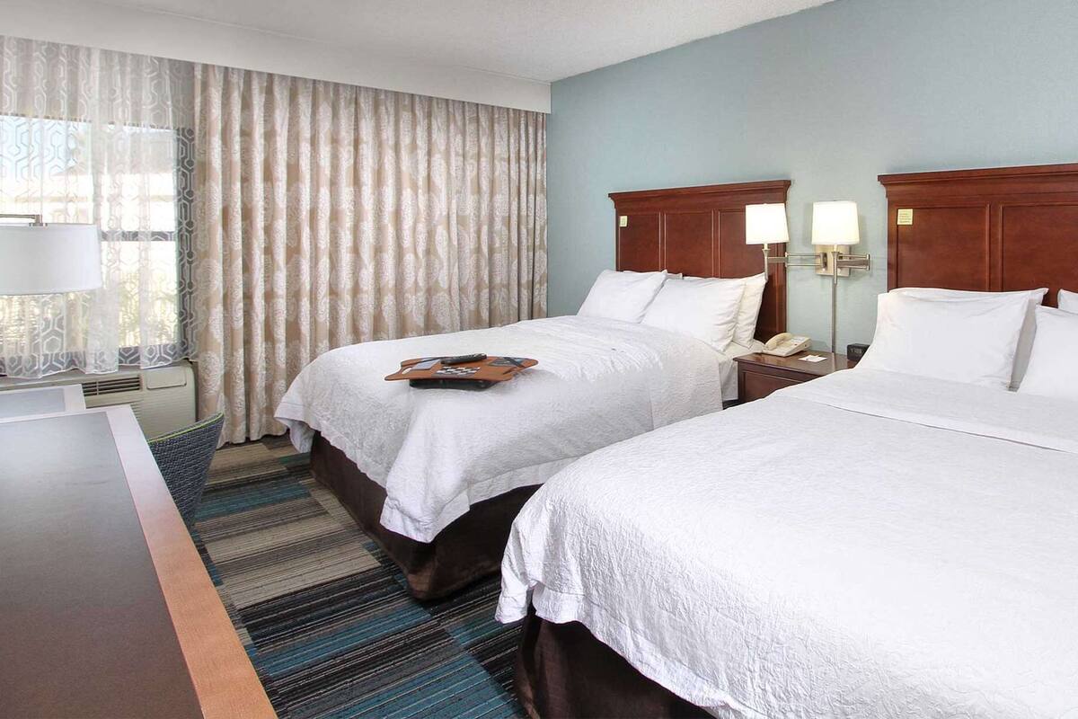 A hotel room with two beds, a desk, a telephone, and a lamp.