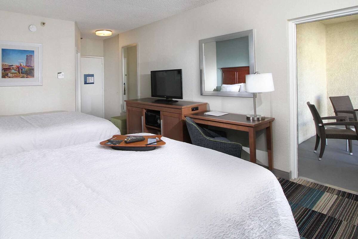 A hotel room with two beds, a desk with a television, a chair, and a small table with a tray.
