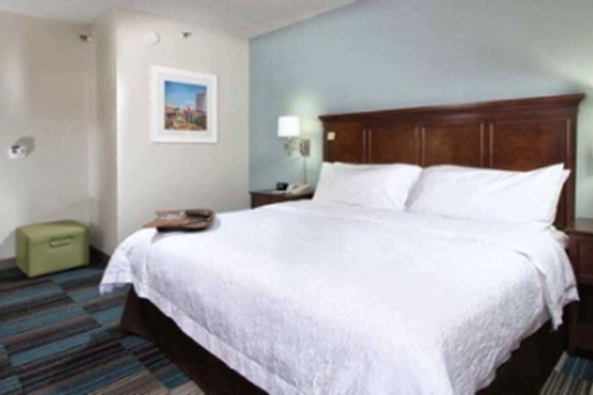 A hotel room with a large bed, a nightstand, a lamp, a picture on the wall, and a suitcase.