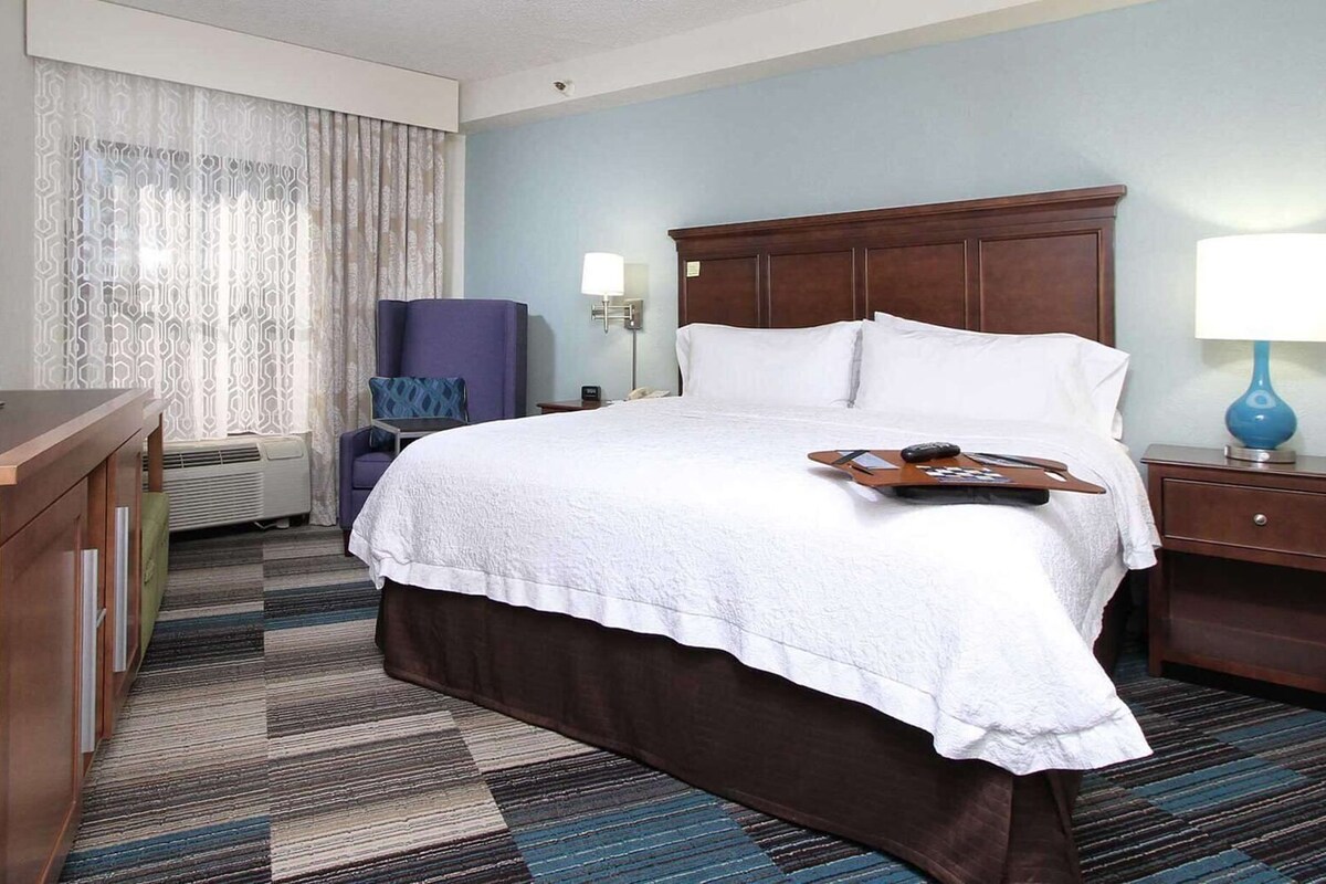 A hotel room with a bed, a television, a desk, a chair, a lamp, and a nightstand.