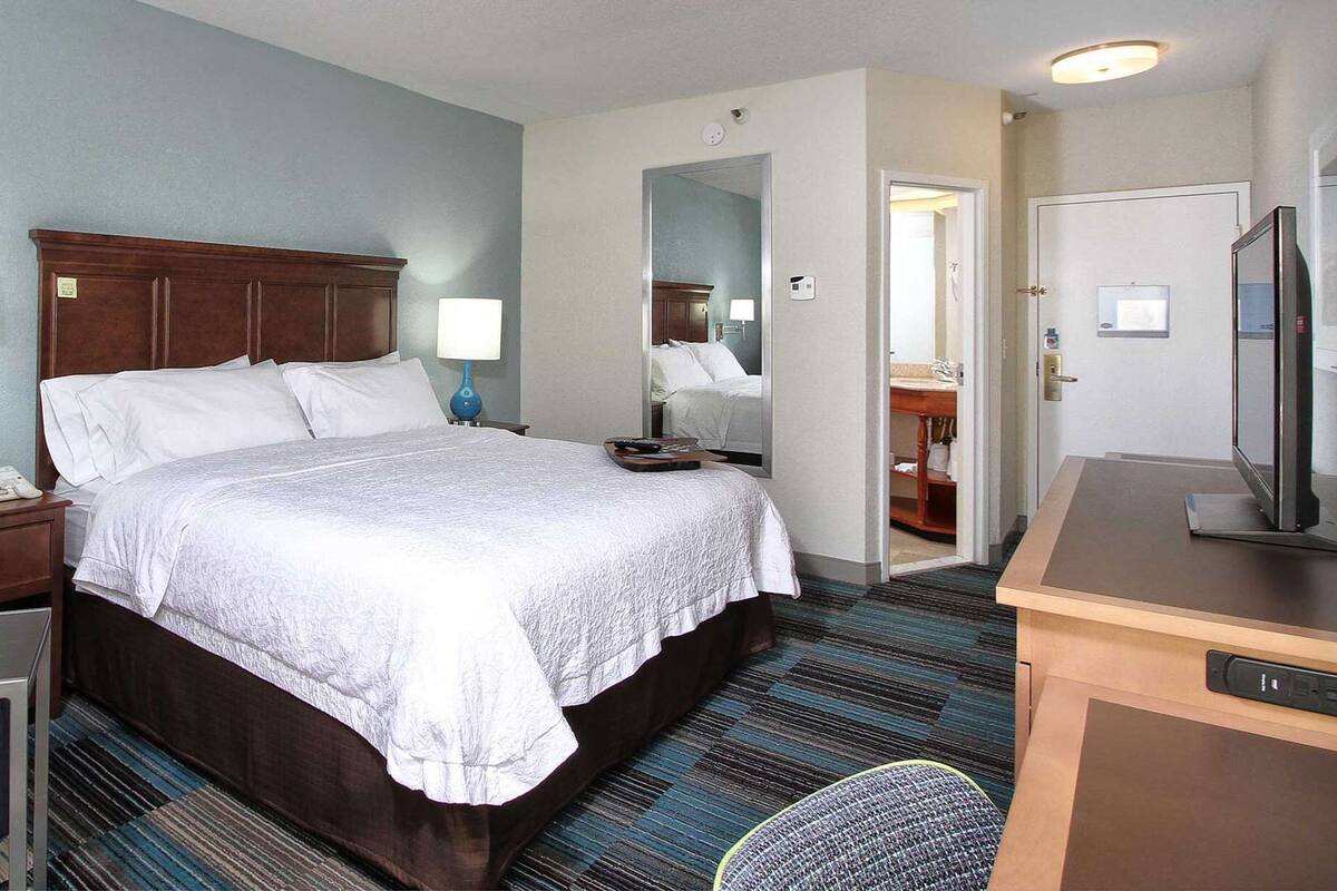 A hotel room with a large bed, a desk with a computer, a chair, and a TV.
