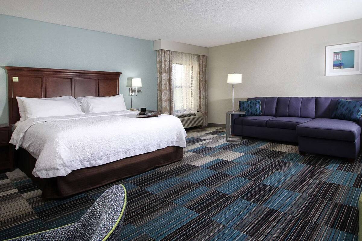 A hotel room with a large bed, a sofa, a desk, and a chair.
