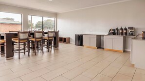 A modern kitchen with a dining area, featuring a large window, a refrigerator, and a coffee station. - Motel 6 Greenwood, MS (Greenwood)