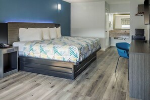 A modern hotel room with a bed, bedside table, and a desk with a chair.