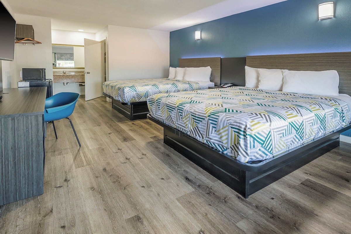 Una habitación de hotel con dos camas, un escritorio, una silla y un televisor.