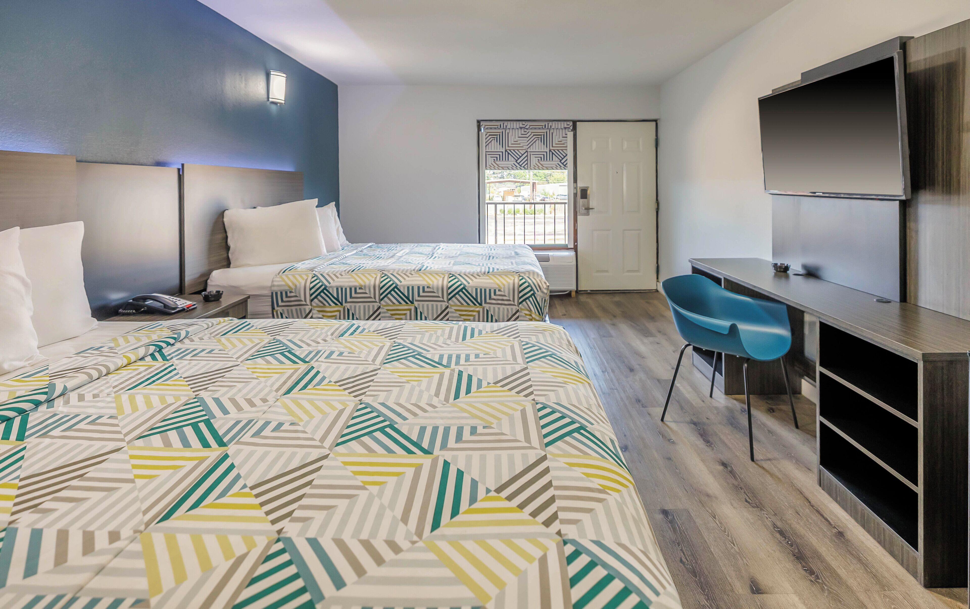 Een hotelkamer met twee bedden, een bureau, een stoel, een televisie en een deur naar buiten.