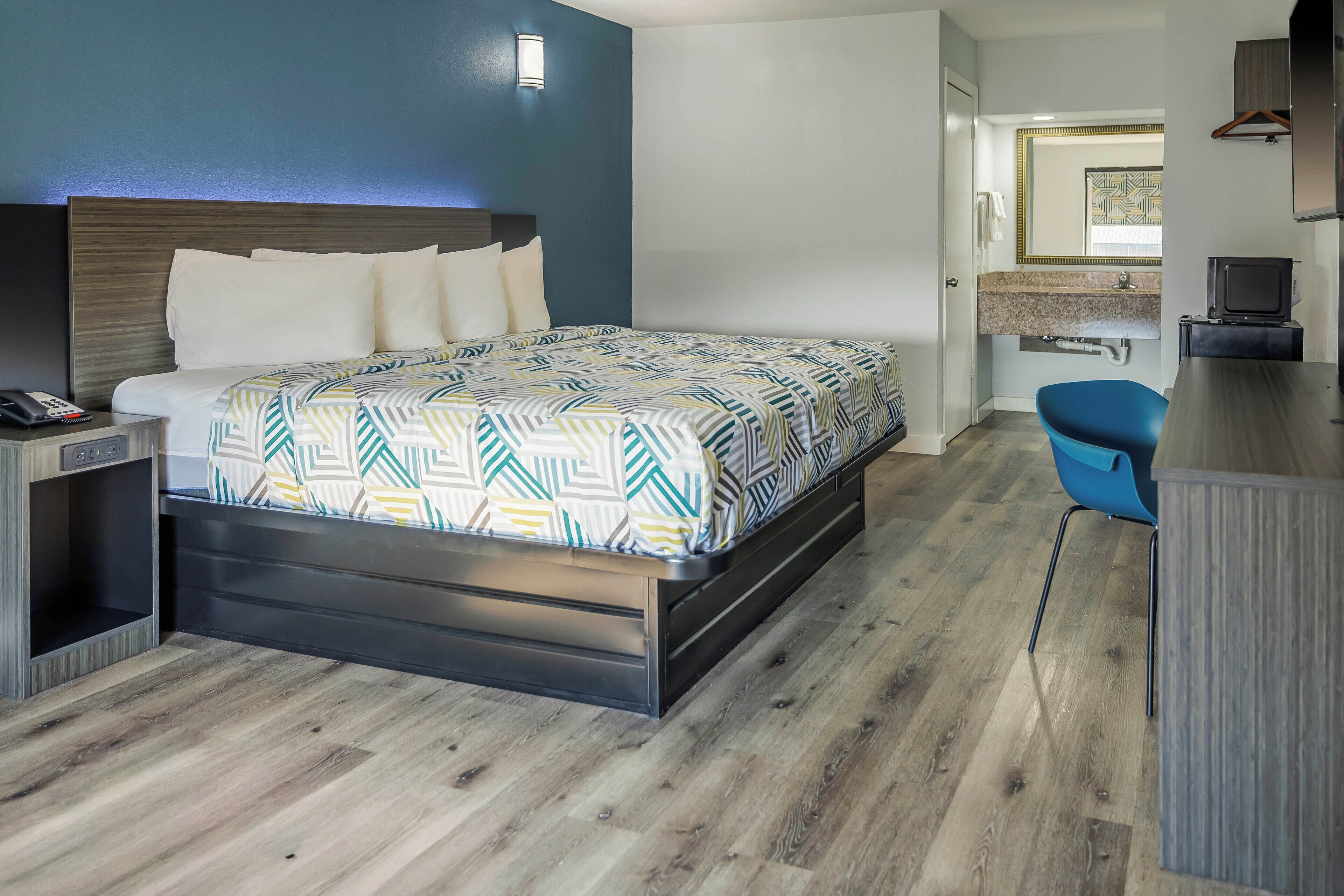Habitación de hotel moderna con una cama grande, un escritorio y un baño visible a través de una puerta abierta.