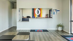 A modern hotel lobby with a reception desk, a seating area with a logo rug, and a potted plant. - Motel 6 Greenwood, MS (Greenwood)
