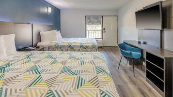 A hotel room with two beds, a desk, a chair, and a TV.