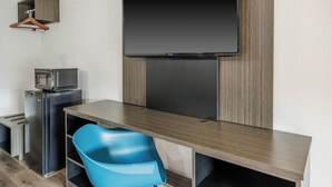A compact room with a flat-screen TV mounted on the wall, a small kitchenette with a microwave, and a blue chair. - Motel 6 Greenwood, MS (Greenwood)