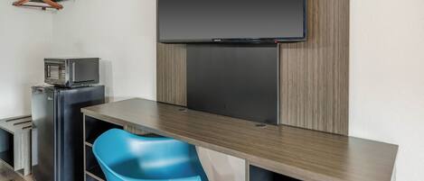 A compact room with a flat-screen TV mounted on the wall, a small kitchenette with a microwave, and a blue chair.