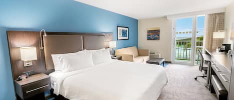 Quarto de hotel com uma cama grande, uma escrivaninha, uma cadeira, uma mesa de cabeceira, uma luminária e vista para o exterior.