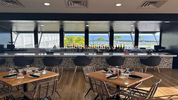 Un restaurant doté d’un bar, de tables avec des chaises et offrant une vue sur l’océan.