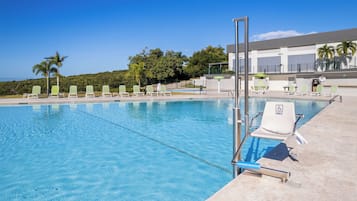 Una piscina amb aigua transparent i blava, envoltada de gandules i un edifici de disseny modern.