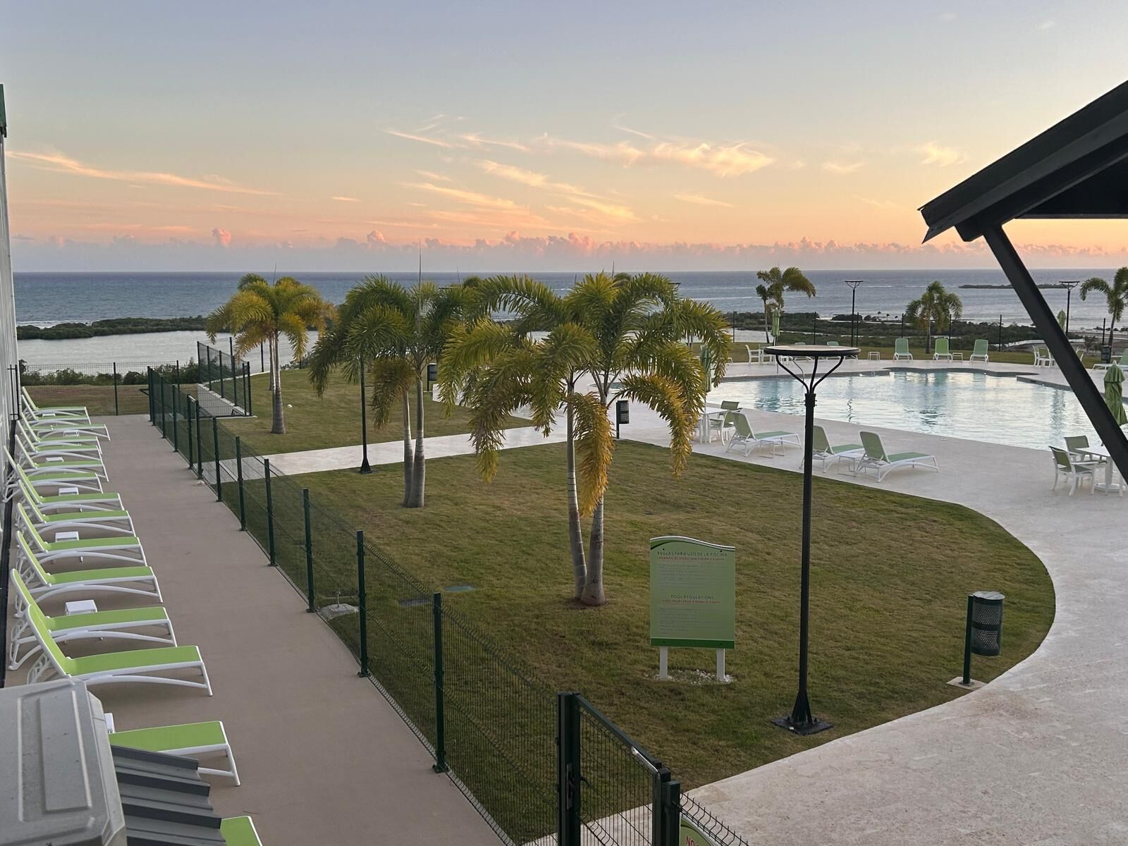 A pool area with lounge chairs, a small pool, and a view of the ocean at sunset.