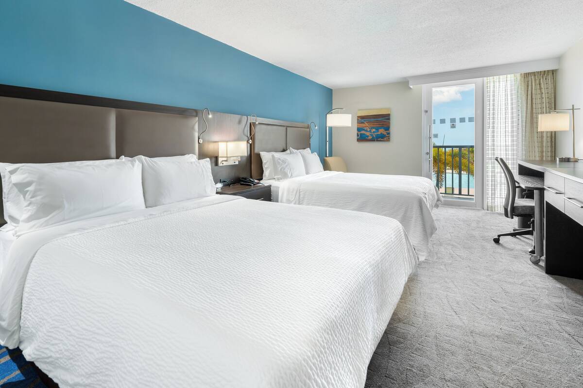 A hotel room with two beds, a desk, and a view of the outdoors.