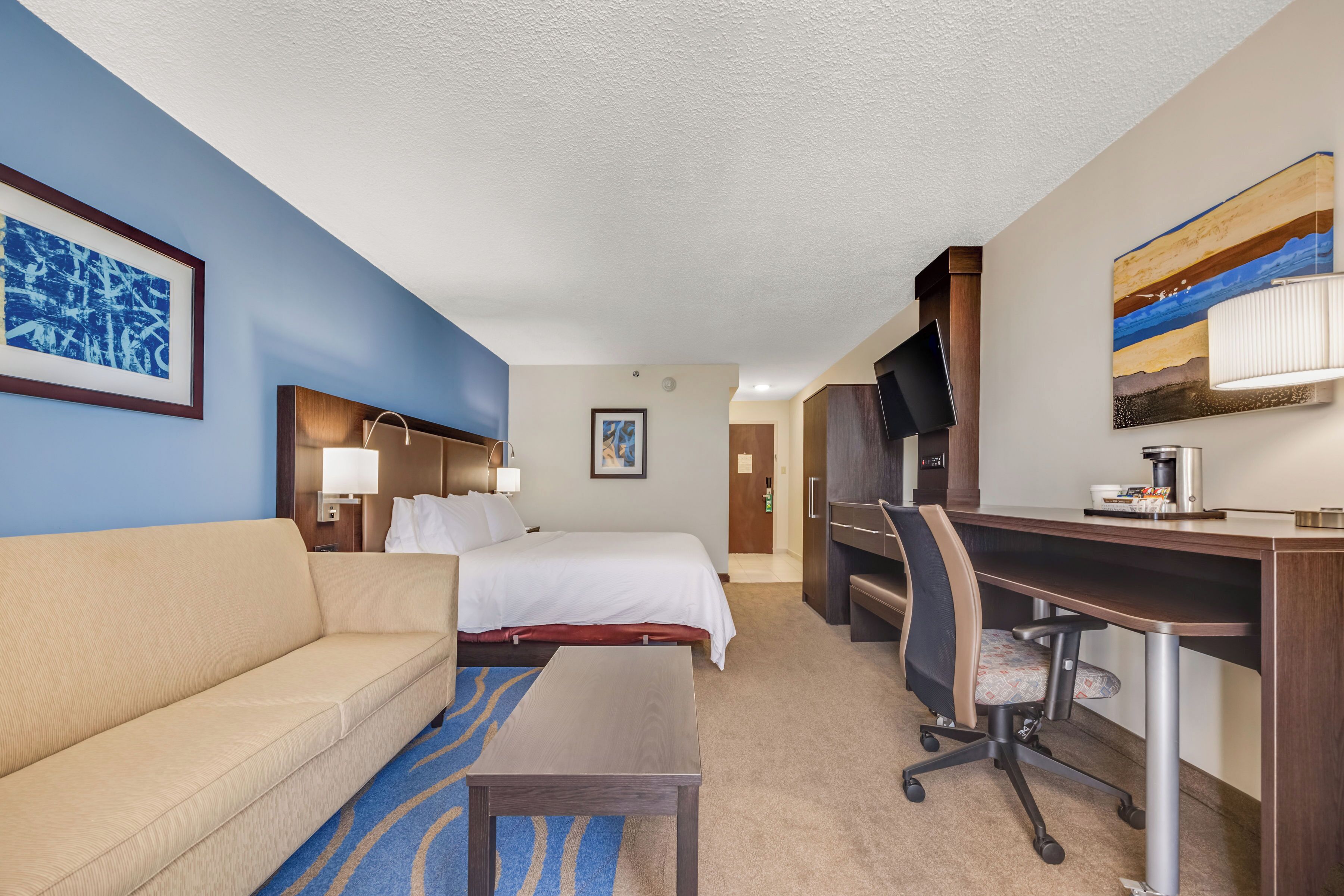 A hotel room with a bed, a desk, a chair, a sofa, and a TV.