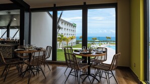 A dining area with wicker chairs and a round table, overlooking a pool and a building with palm trees. - Holiday Inn Ponce & Tropical Casino by IHG (Ponce)