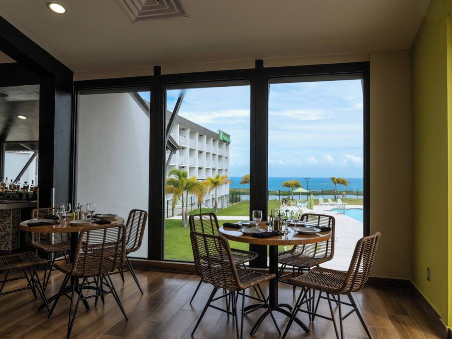 A dining area with wicker chairs and a round table, overlooking a pool and a building with palm trees.