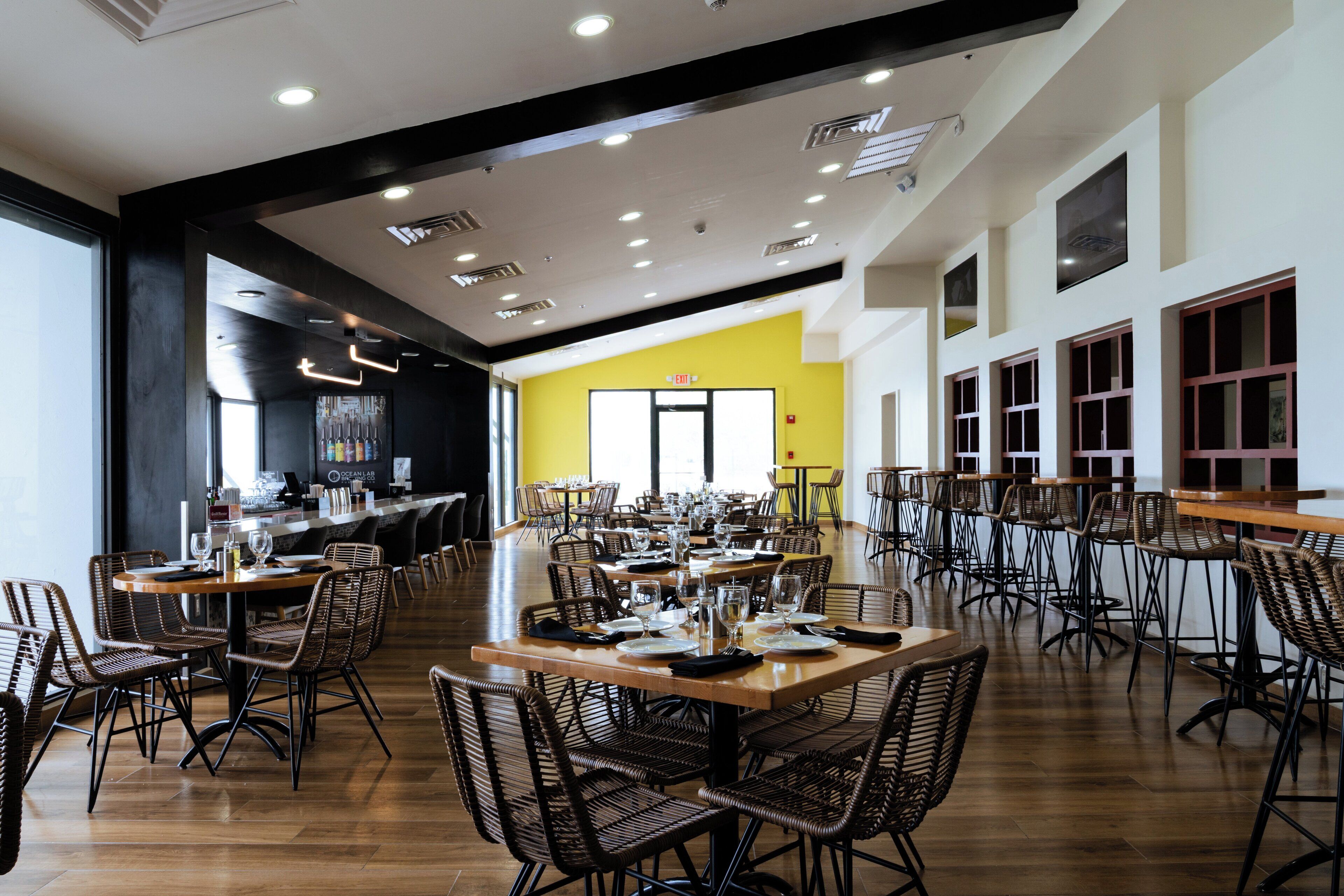 A spacious dining area with multiple tables and chairs, a bar counter, and a bright yellow accent wall.