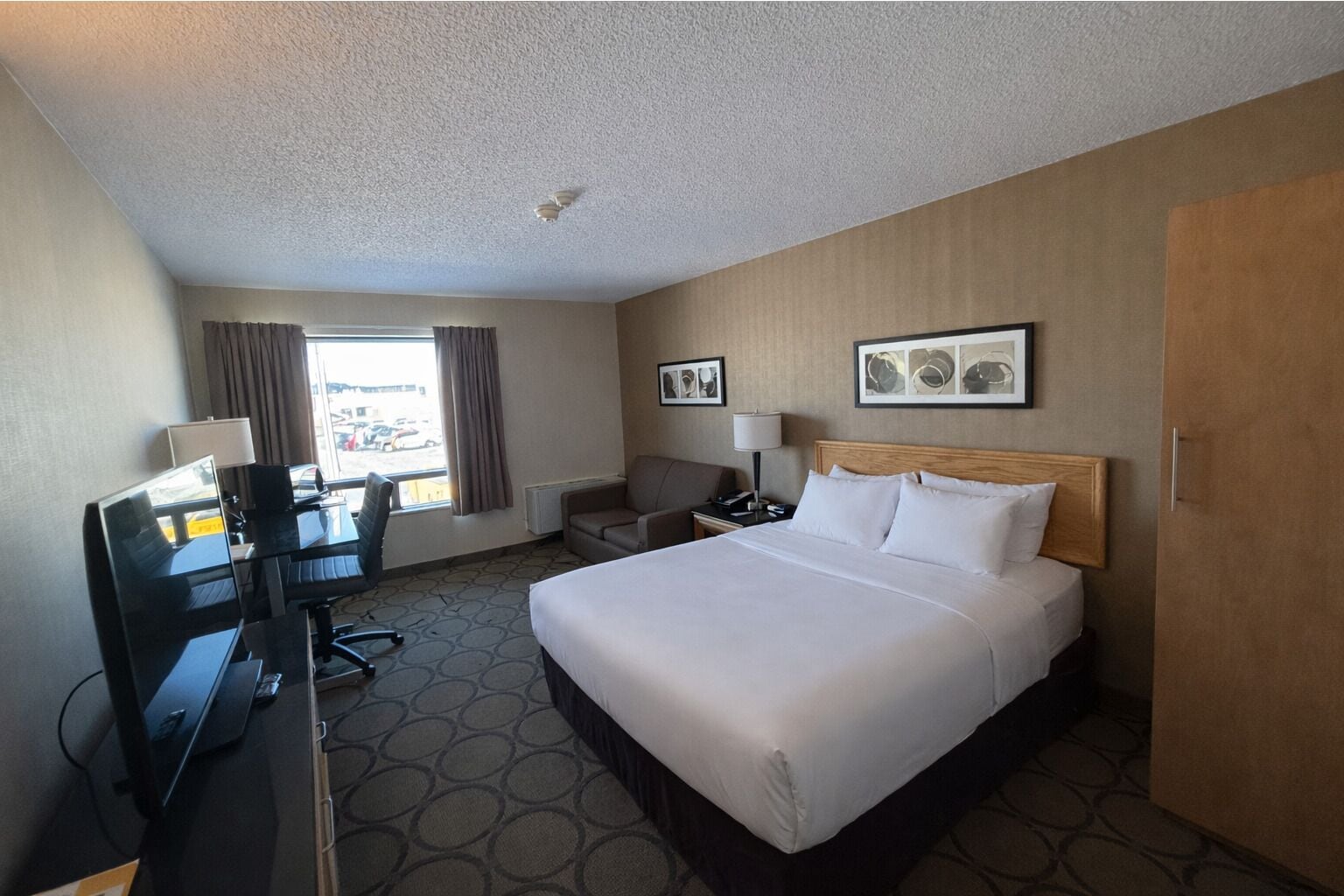 A hotel room with a large bed, a desk with a computer, a chair, and a window with curtains.