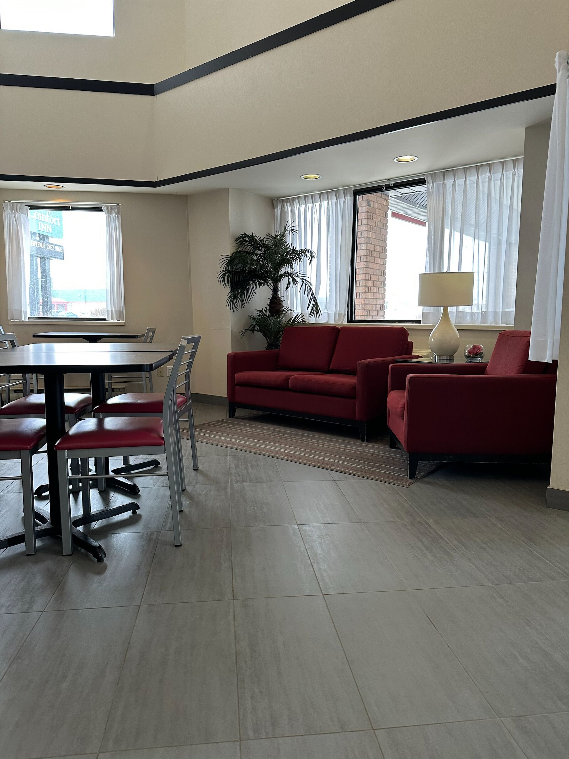 A modern living room with a red sofa, a dining table with chairs, and a large window with curtains.
