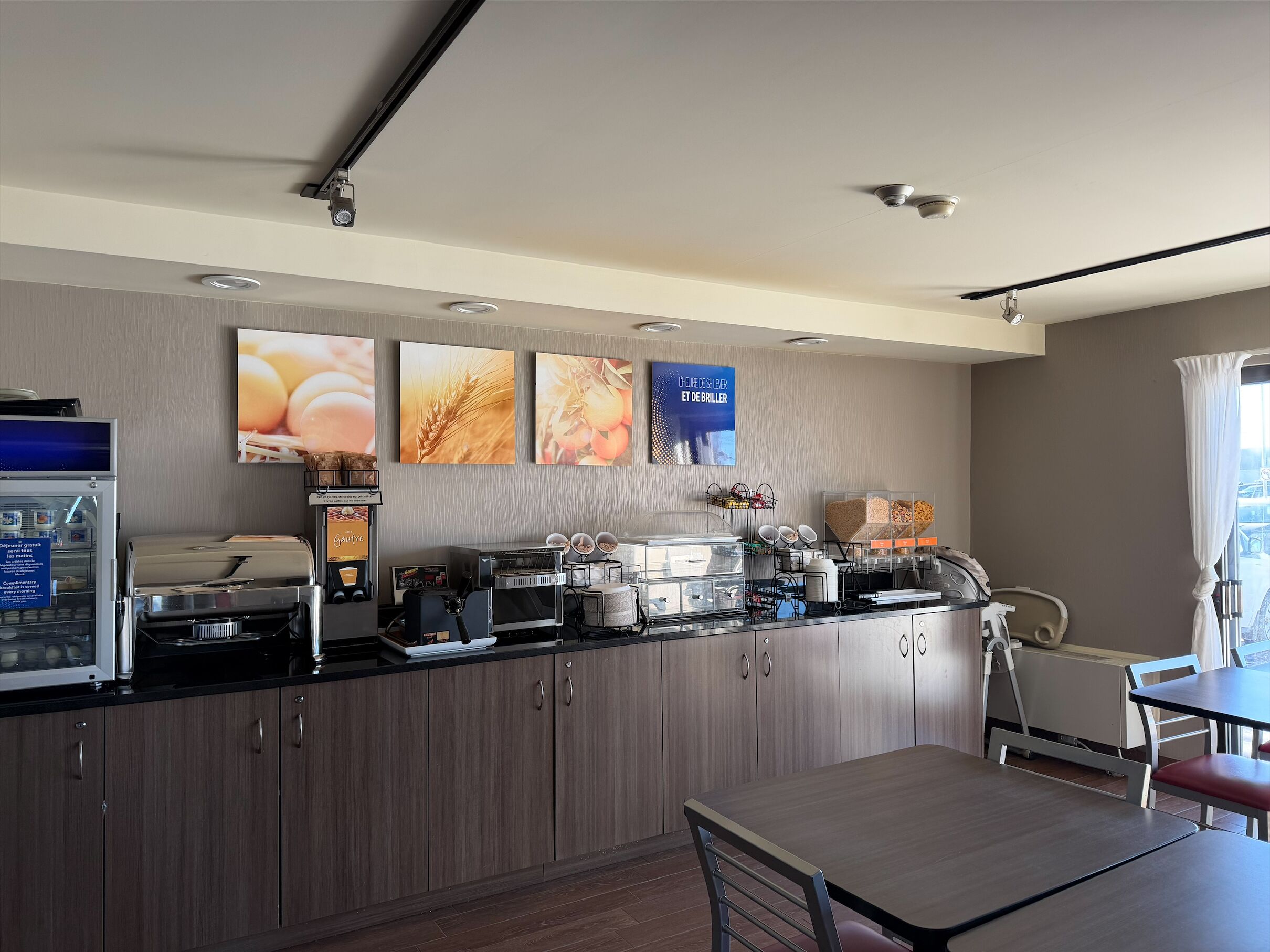 A modern kitchen with a coffee machine, bread display, and a dining area with a table and chairs.