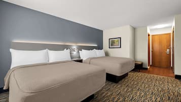 Habitación de hotel con dos camas, una mesita de noche, una lámpara, un cuadro enmarcado en la pared y una puerta que conduce a otra habitación.