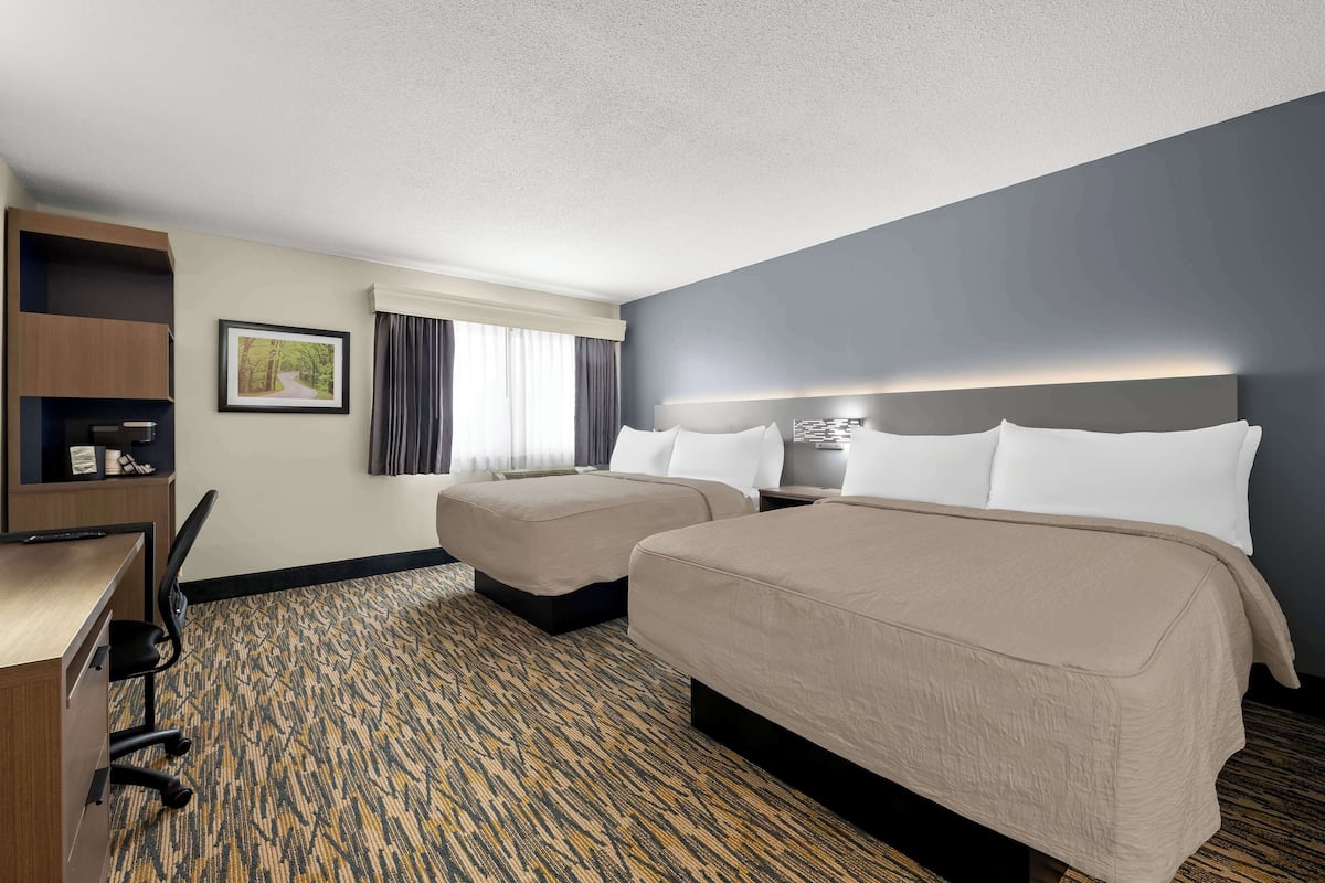 A hotel room with two beds, a desk, a chair, a picture on the wall, and a window with curtains.