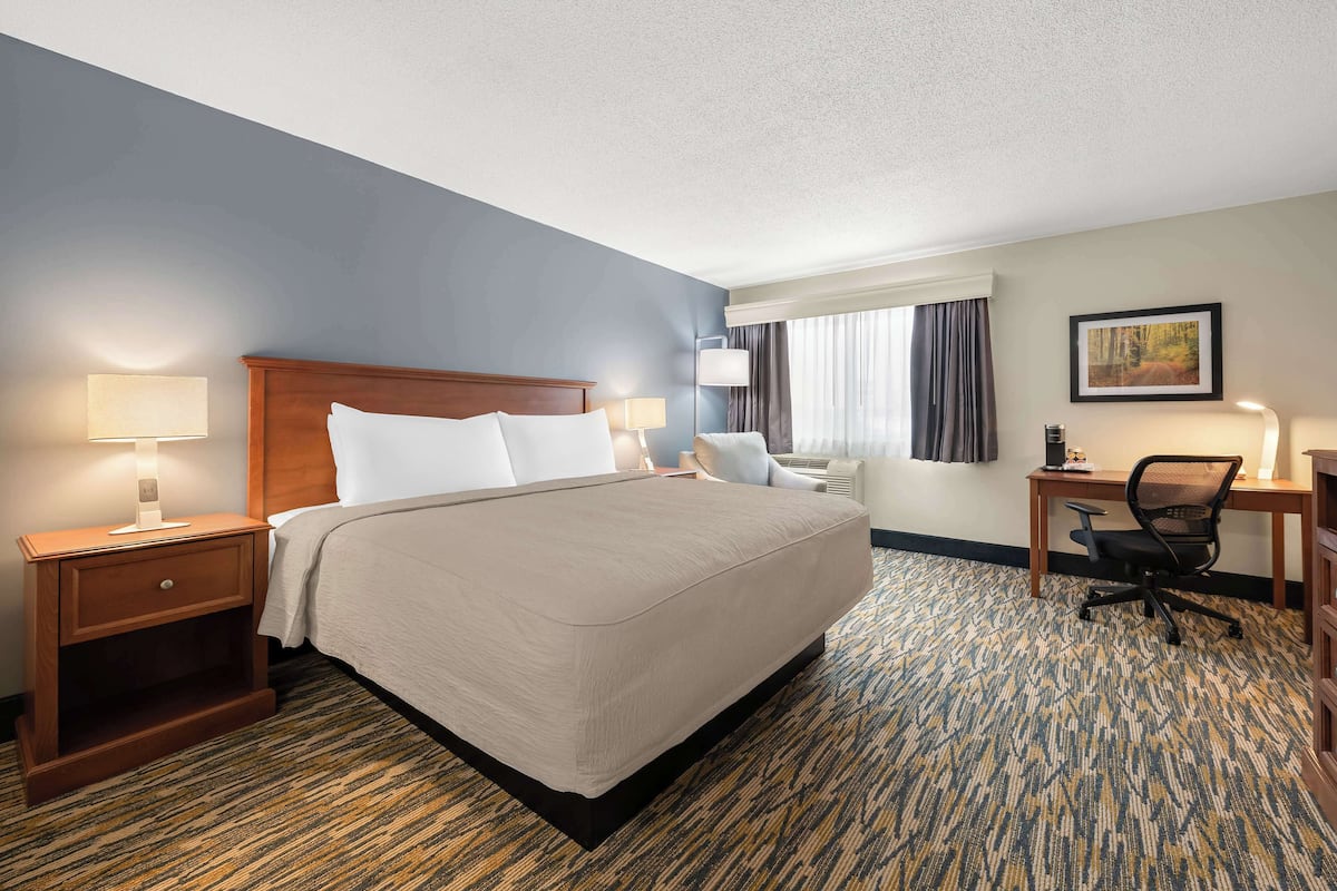 A hotel room with a large bed, a desk, a chair, and a nightstand with lamps.