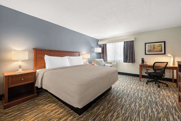 A hotel room with a large bed, a desk, a chair, and a nightstand with lamps. - Best Western Inn (Rice Lake)