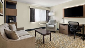 Une chambre d’hôtel équipée d’un canapé, d’un fauteuil, d’un bureau et d’un téléviseur à écran plat.