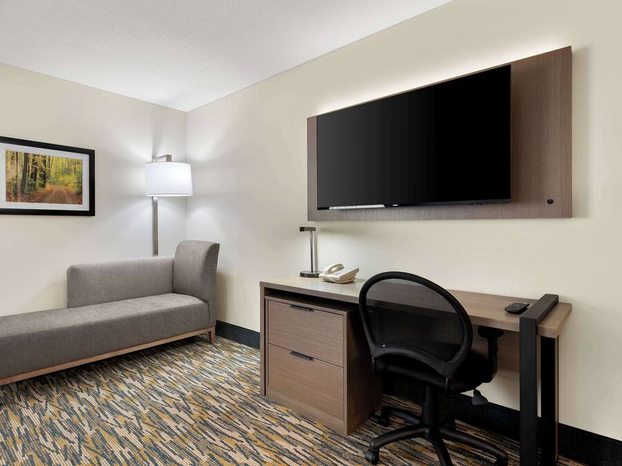 Ett hotellrum med en soffa, ett skrivbord, en stol, en platt-TV, en lampa och en inramad tavla på väggen.