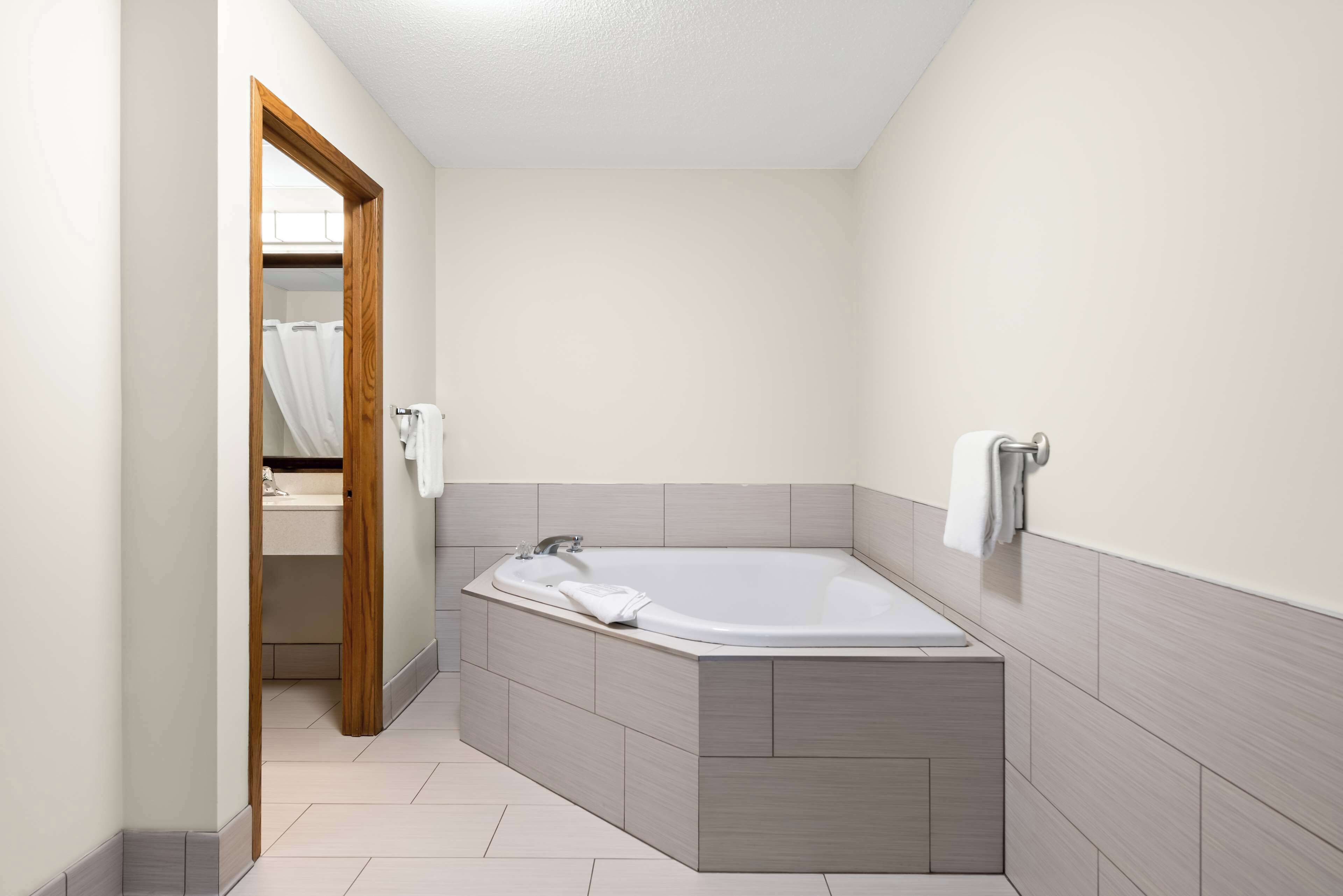 Un baño moderno con una bañera independiente, una puerta de madera que da a un vestidor y un perchero en la pared.