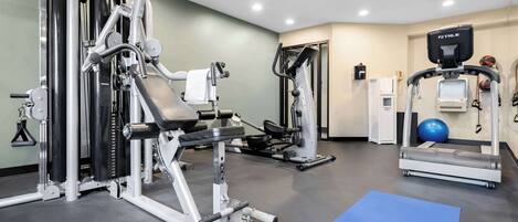 A gym with various exercise equipment, a blue mat, and a white towel on the floor.