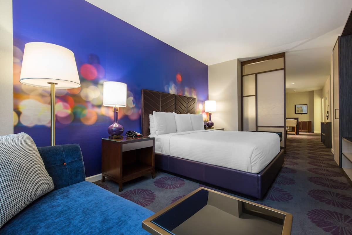 A hotel room with a bed, a sofa, a nightstand, and a lamp.
