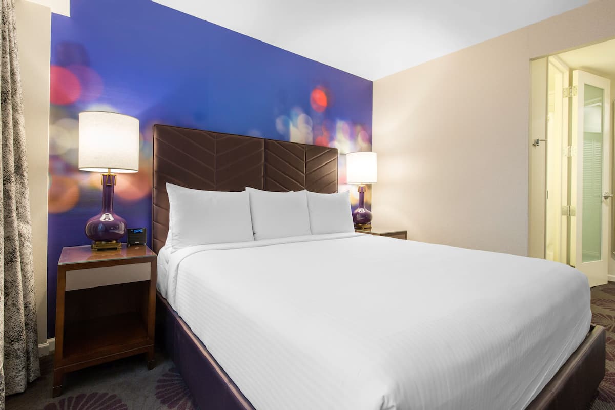 A hotel room with a large bed, two bedside tables with lamps, a door, and a wall with a bokeh light effect.