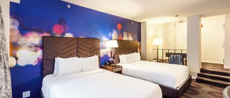 Habitación de hotel con dos camas, una pared azul con efecto bokeh de luces y piso alfombrado.