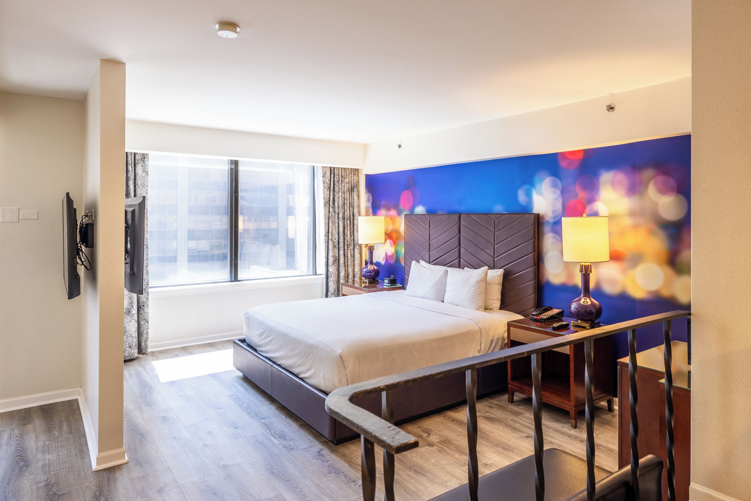 A hotel room with a large bed, a desk, a chair, a TV, and a window with curtains.