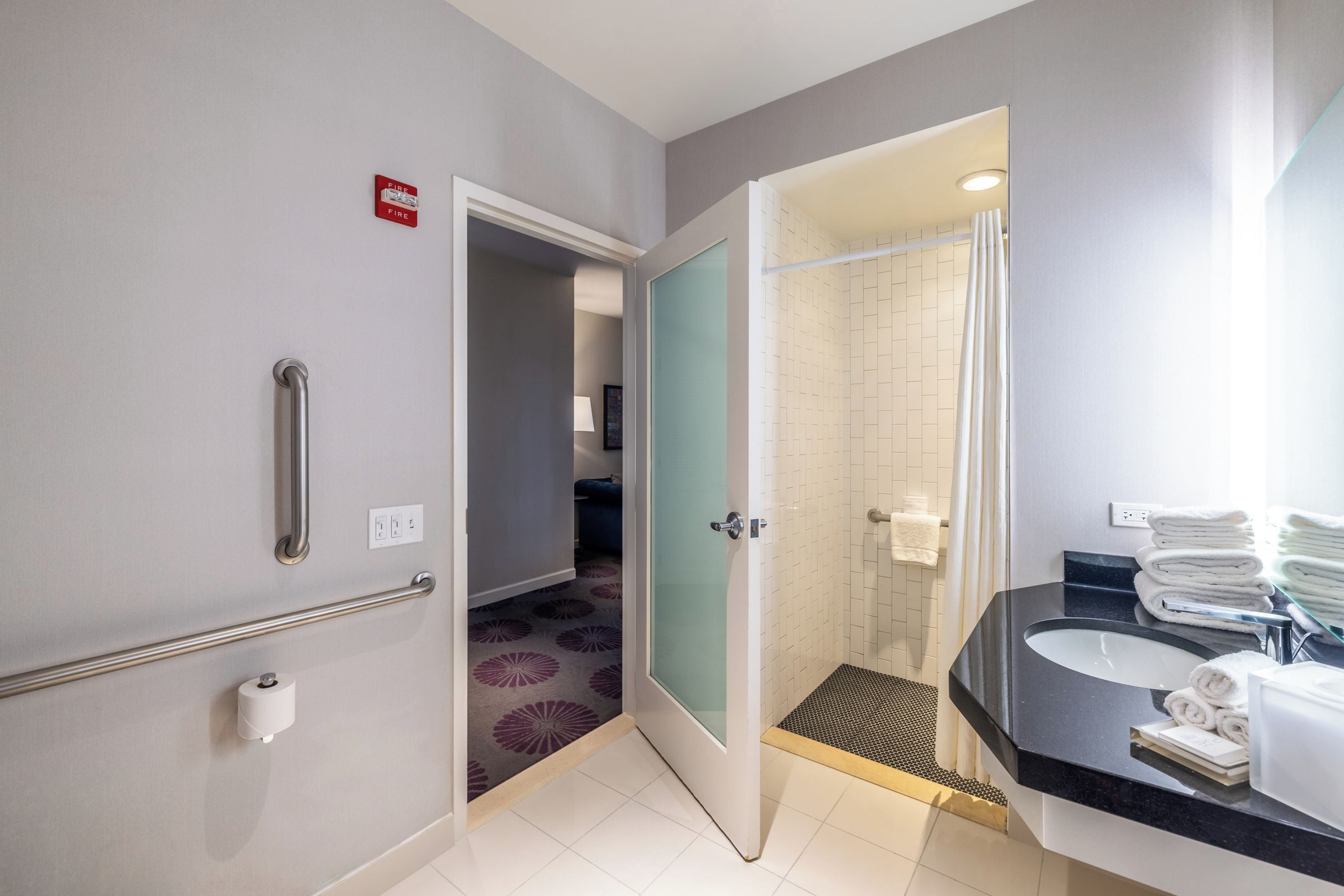 A modern bathroom with a shower, a sink with towels, and a handrail.
