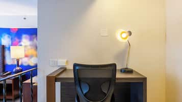 A hotel room with a desk, a chair, a lamp, and a wall socket.