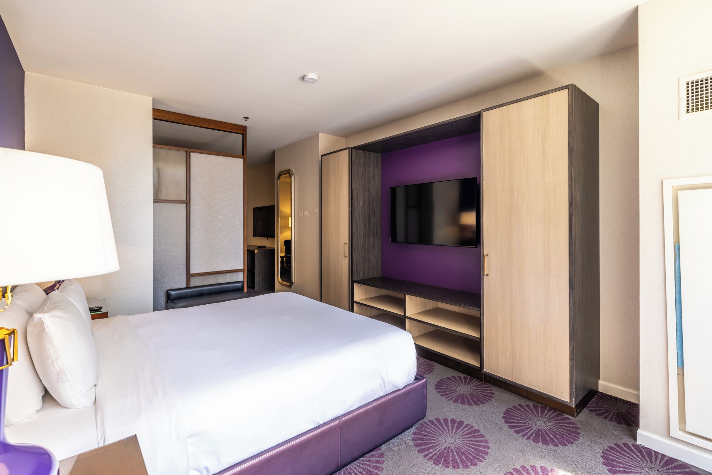 A hotel room with a large bed, a TV mounted on the wall, and a wardrobe with open doors.