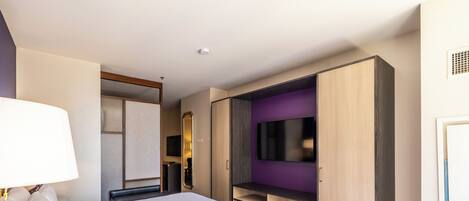 A hotel room with a large bed, a TV mounted on the wall, and a wardrobe with open doors.
