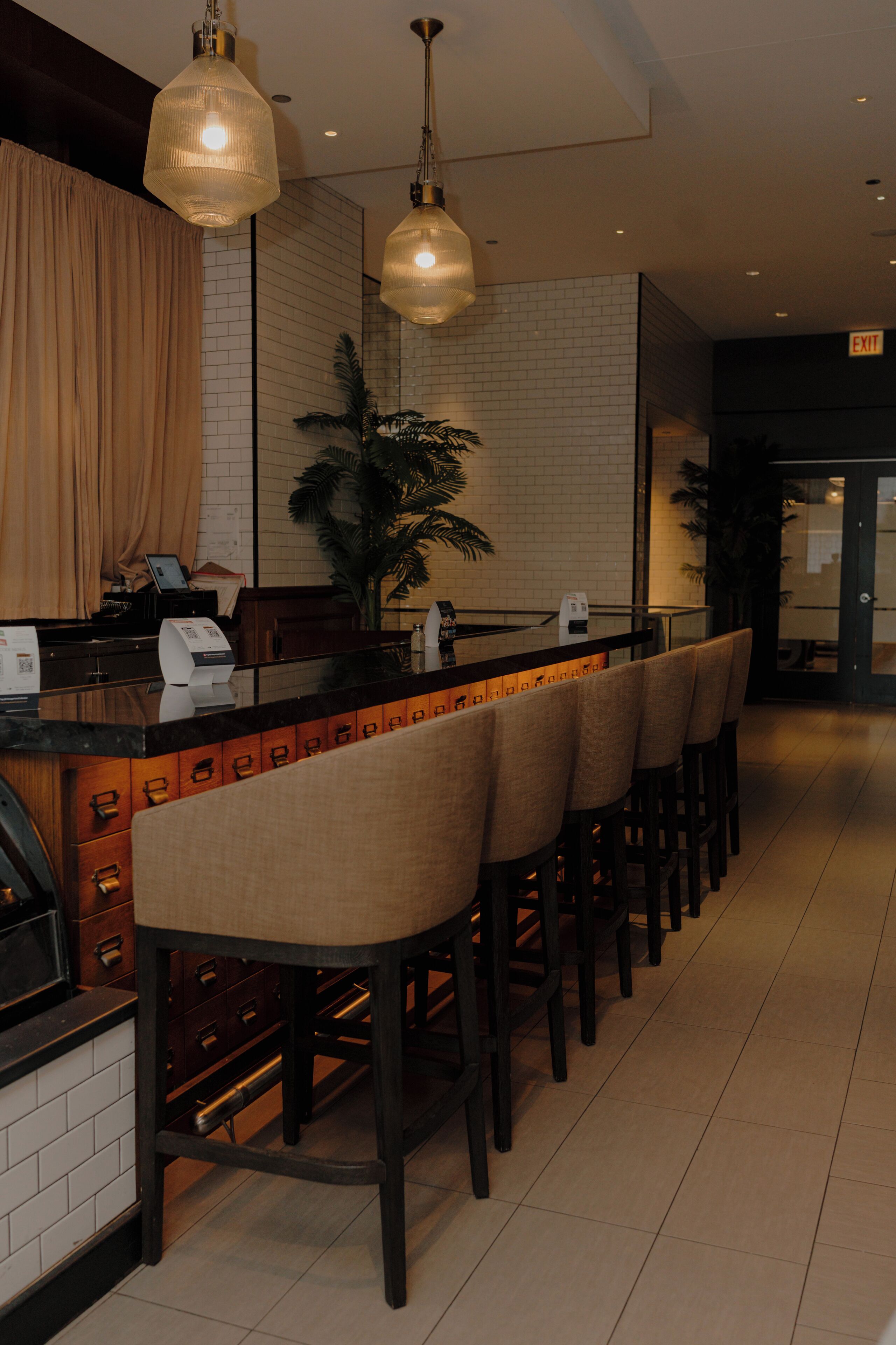 A bar area with a long counter, multiple stools, and pendant lighting.